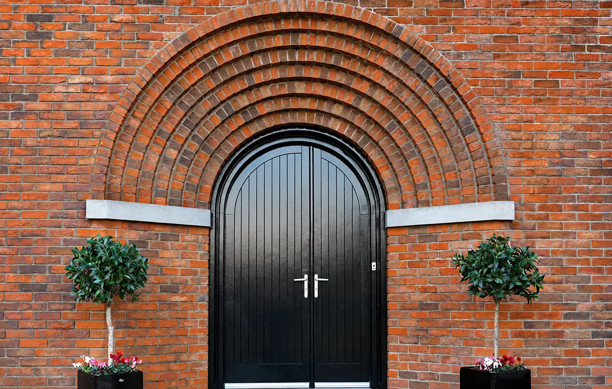 Brick arch over arched black double doors