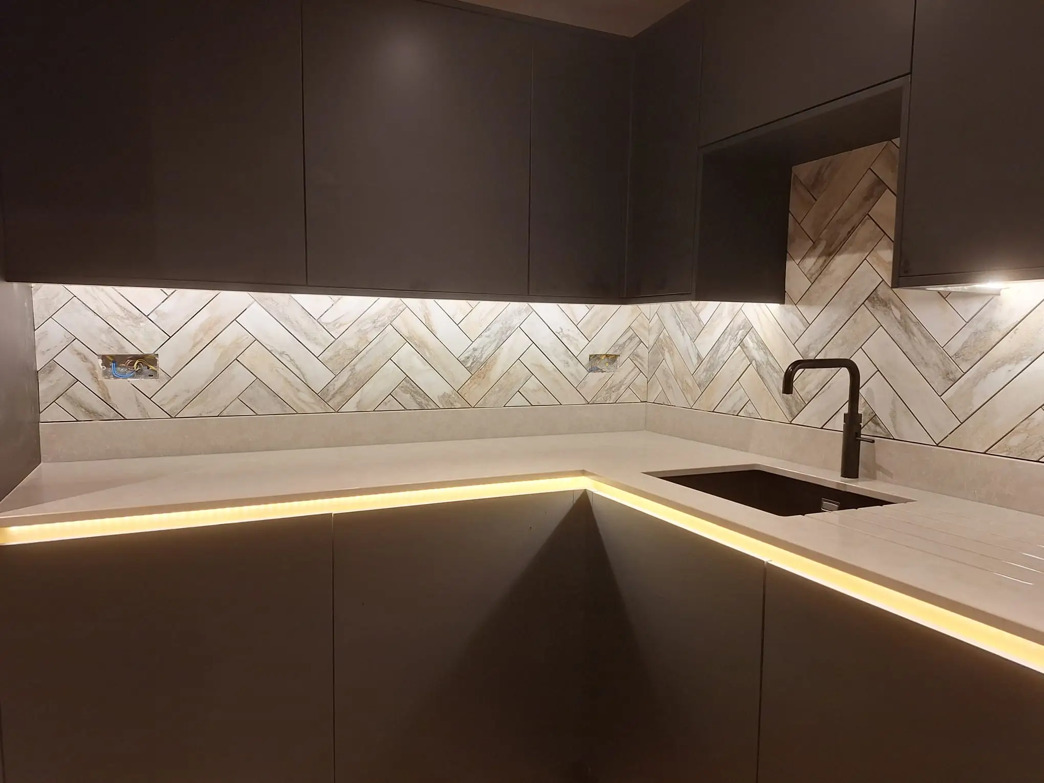 Dark kitchen with lit plinths and a herringbone splashback