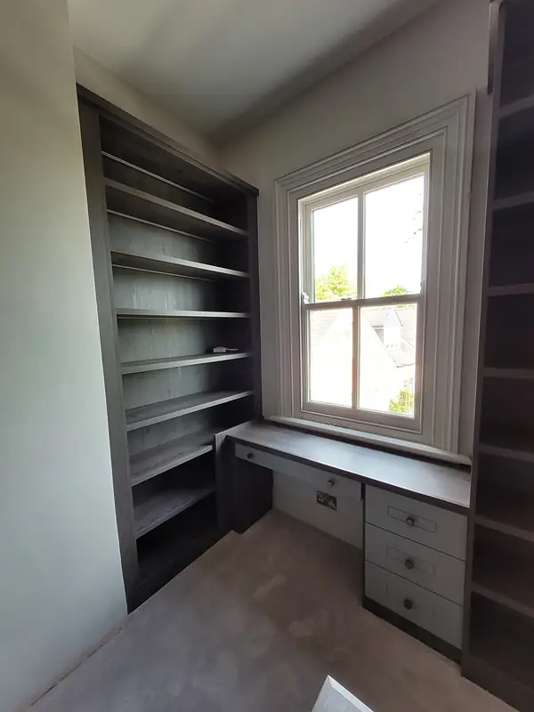 Fitted desk and shelving beside a sash window