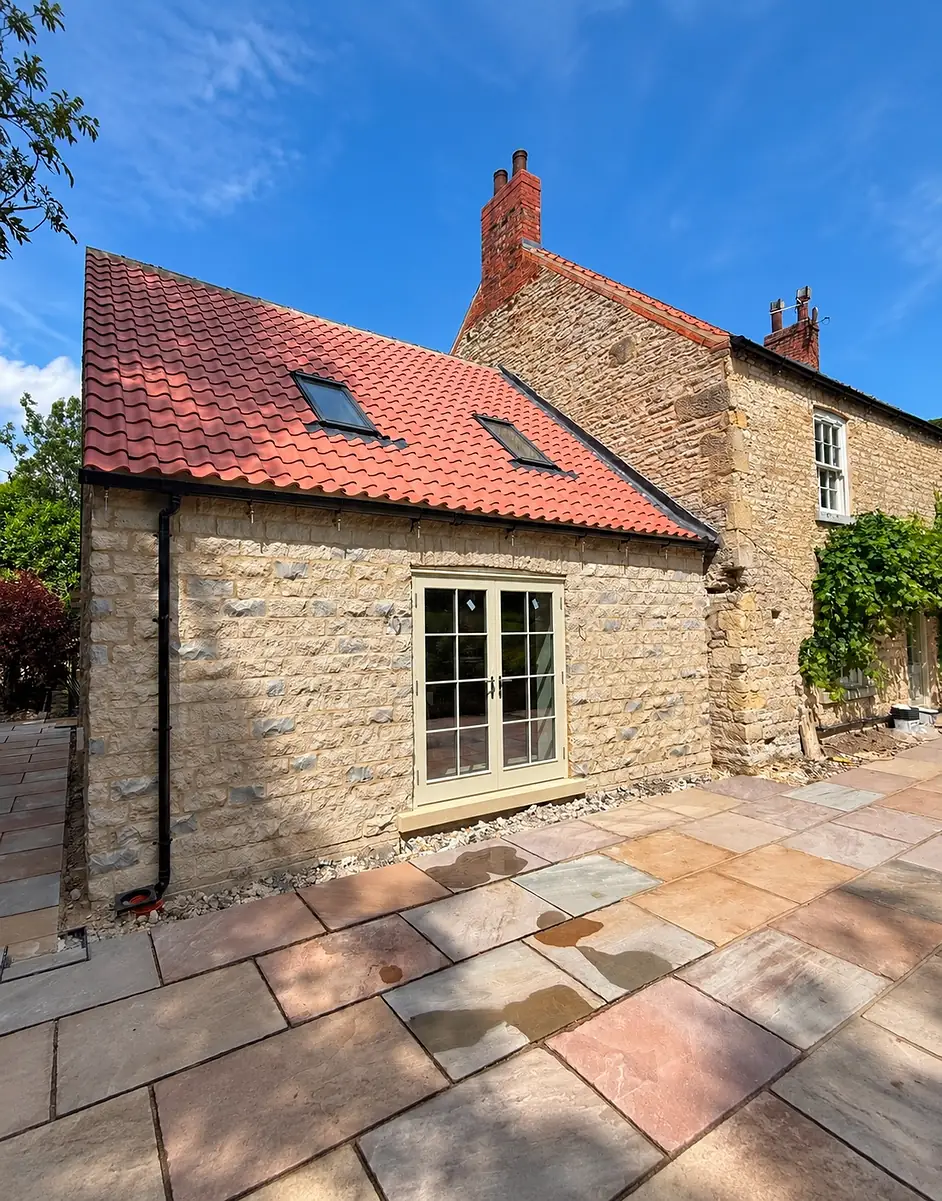 The finished stone extension with a pantile roof, French doors and a sandstone patio
