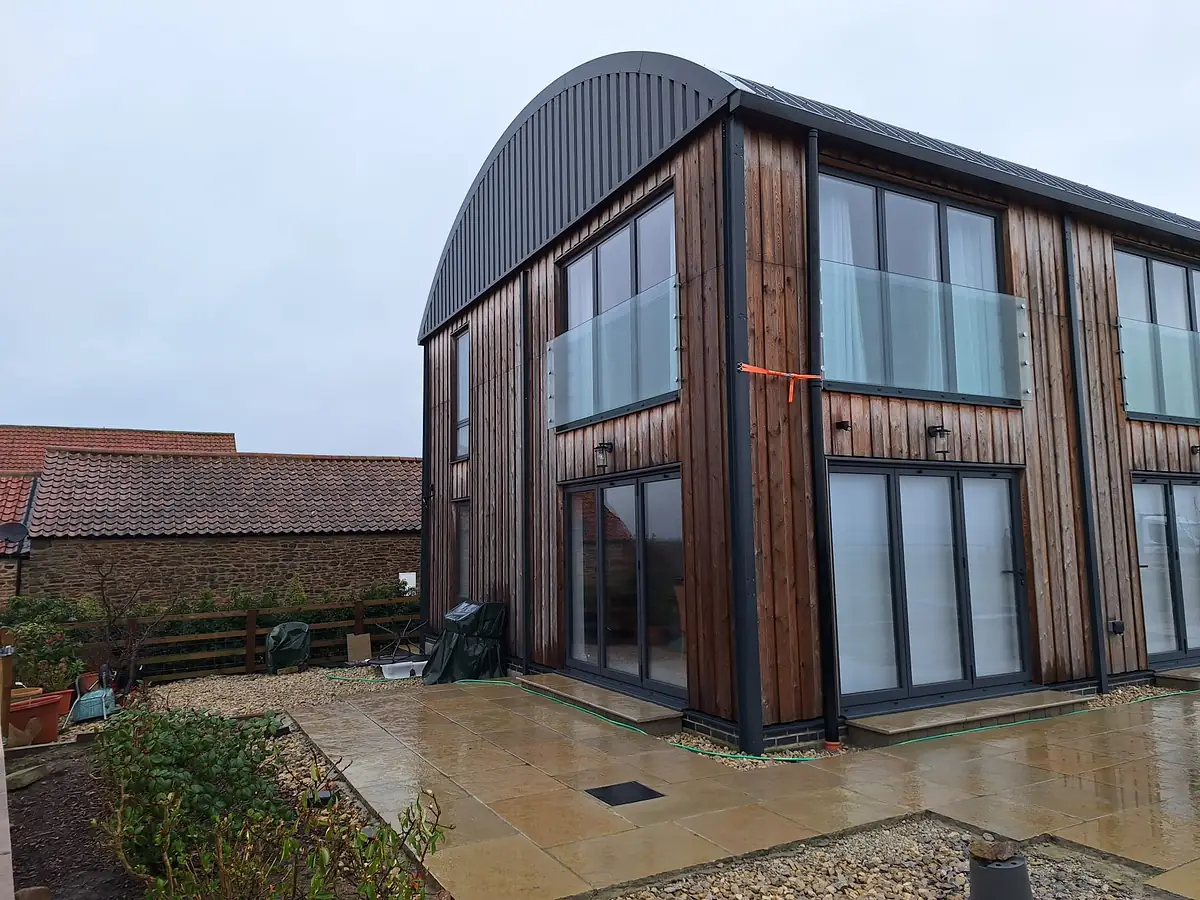 Timber clad Dutch barn house at Whenby with a curved roof and glazed gable